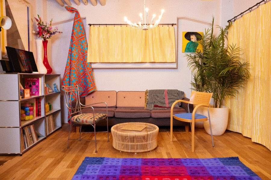 Cozy retro living room with a beige sofa, wicker coffee table, and bright yellow striped curtains under a chandelier.