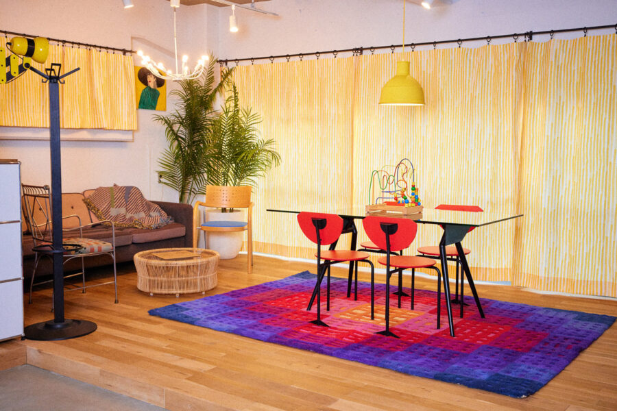 Cozy, colorful dining and living space with a glass table, red chairs, a vibrant purple-blue rug, and a bead maze toy on the table.
