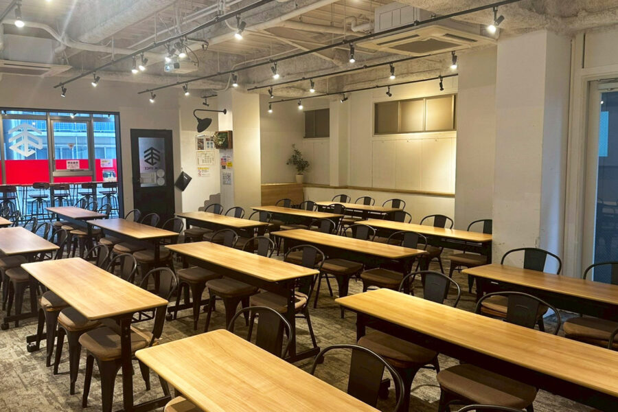Industrial-style cafe interior with long wooden tables and black metal chairs under track lighting.