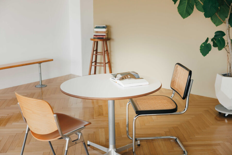 A round white table with two chairs in a bright minimalist room and a plant in a white pot nearby