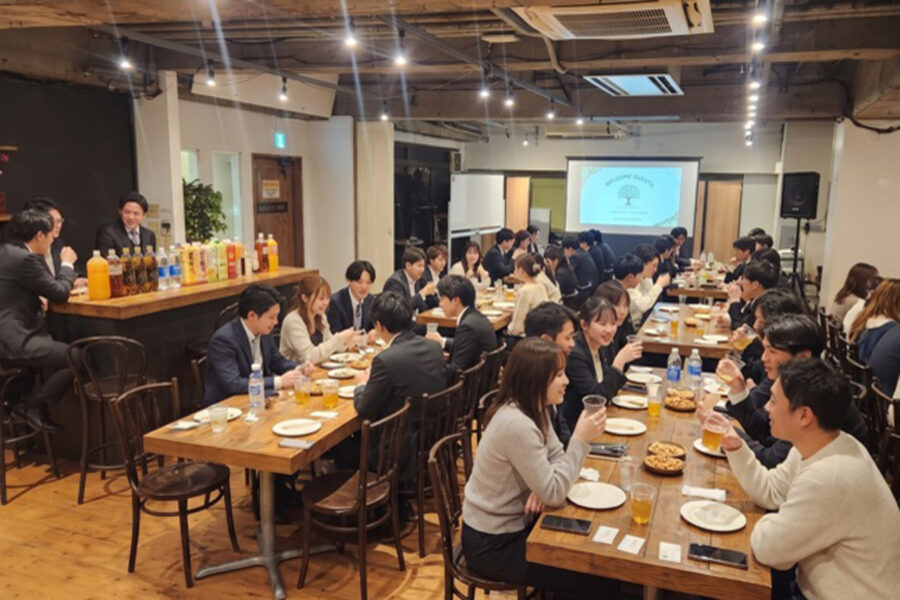 Large group of professionals dining at long wooden tables in a restaurant, raising glasses in a toast.