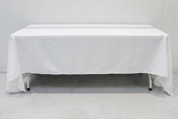 Rectangular table covered with a white tablecloth in a plain studio setting.