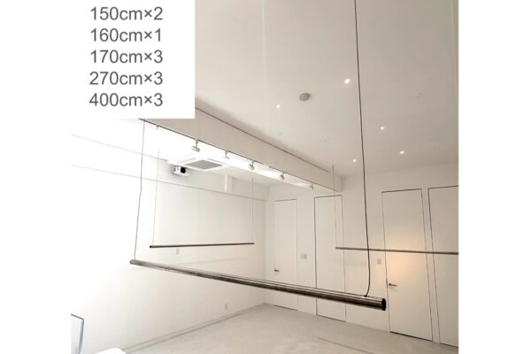 White dance studio with a mirrored wall and a long ceiling-hung ballet barre for practice.