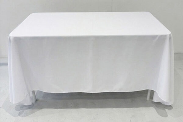 A rectangular table covered with a white tablecloth in a neutral studio setting, with the cloth draping to the floor on all sides.