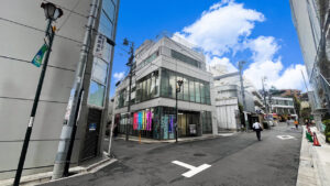 Modern glass-fronted building on a quiet city street; neon signs glow in the storefront windows.