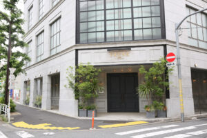 Stone-front building with a black double door entrance labeled 'TRUNK', flanked by potted plants on a city street with a crosswalk nearby.