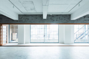 Empty white industrial loft with large floor-to-ceiling windows and a metal staircase outside to the right.