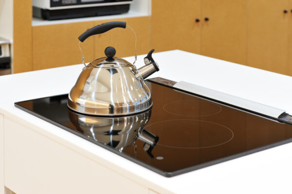 Stainless kettle with black handle on a glass induction cooktop in a bright kitchen.
