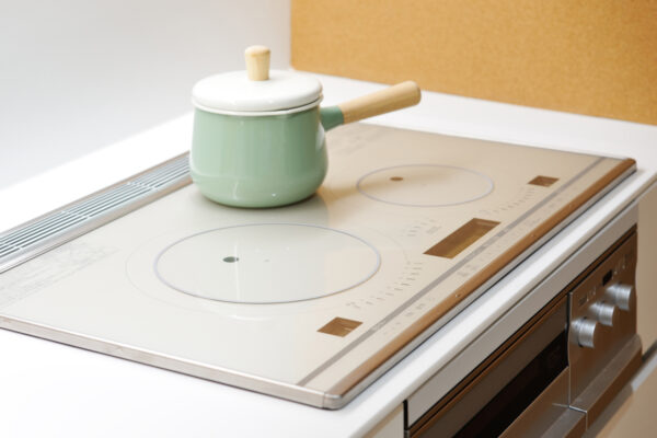 Mint green pot with a wooden handle and lid sits on a white electric induction cooktop in a modern kitchen.