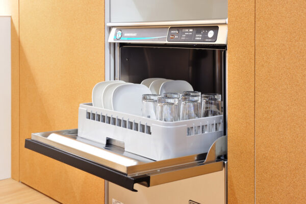 Open dishwasher with a loaded rack of plates and glasses ready to be washed in a modern kitchen.