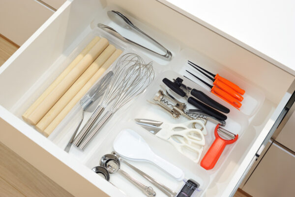 Organized kitchen utensil drawer with wooden rolling pins, whisks, tongs, scissors, and corkscrew tools neatly arranged