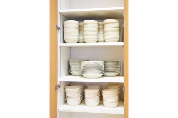 Open cabinet filled with stacks of white bowls and plates on three shelves, organized by size.