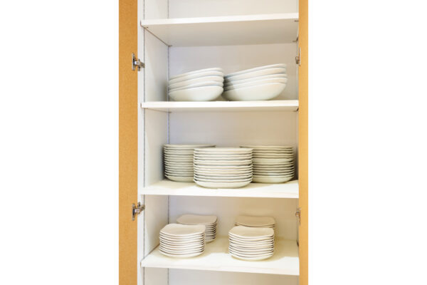 Open kitchen cabinet with three shelves of white dishes neatly stacked (bowls on top, plates in the middle and bottom).