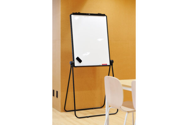 Whiteboard on a black metal easel in a room with an orange wall and light wooden floor, with an eraser and marker on the tray.