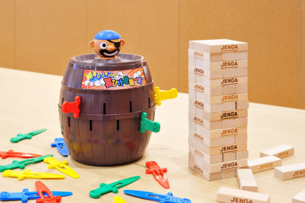 Plastic pirate barrel game on a table with a blue-capped pirate head and colorful clamps beside a tall Jenga tower.