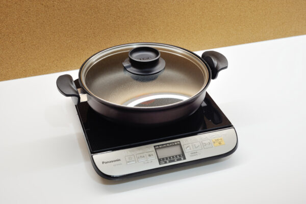 Panasonic induction cooktop with a black pot and clear glass lid on a white countertop.
