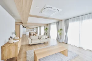 Bright open-plan living room with a beige sofa, wooden coffee table, and a light shag rug by tall windows with gray curtains.