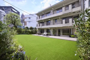 Apartment building with balconies overlooking a well-kept lawn and patio seating area outdoors