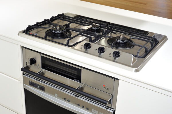 Stainless steel gas range with four burners and a built-in oven beneath in a white kitchen.