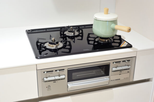Green enamel pot with a wooden handle on the front-right burner of a black gas cooktop above a built-in oven in a modern kitchen, lid on top.