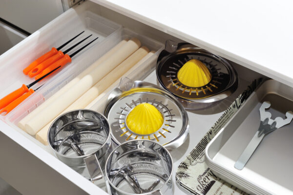 107 Open kitchen drawer with orange-handled skewers, wooden rolling pins, and metal citrus juicers.