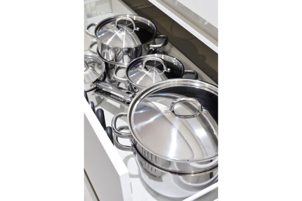110 Set of stainless steel pots with lids stacked in an open kitchen cabinet drawer.