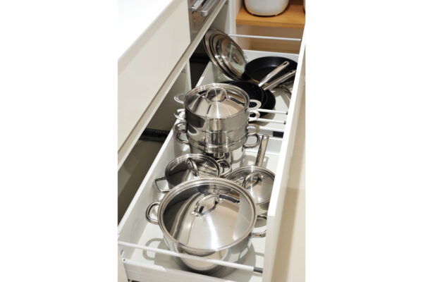 Pull-out kitchen cabinet drawer filled with stacked stainless steel pots and pans with lids visible.