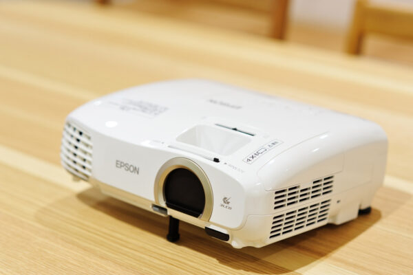 White Epson projector resting on a wooden floor, lens facing forward. (Informative, concise)