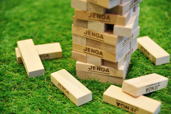 Tall Jenga tower made of wooden blocks on a green lawn, with several blocks scattered nearby.