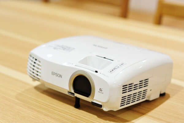 117 White Epson projector sits on a light wooden floor, lens visible in front and vents on the side.