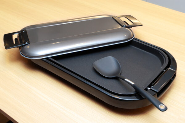 118 Electric grill sandwich press with lid open and a spatula resting inside on a wooden table surface