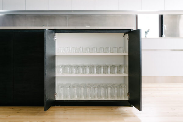 Open kitchen cabinet with three white shelves neatly filled with clear glass jars on a wooden floor
