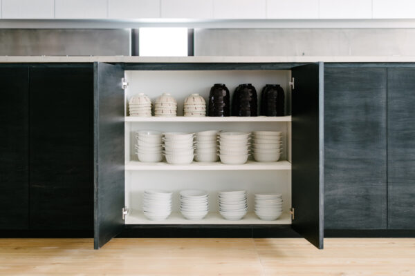Open cabinet with three shelves: top row has white bowls on the left and black bowls on the right; middle and bottom rows contain white bowls.