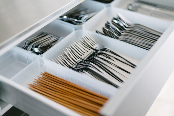 Drawer of organized cutlery with forks and spoons in white compartments, plus brown chopsticks in a separate section.