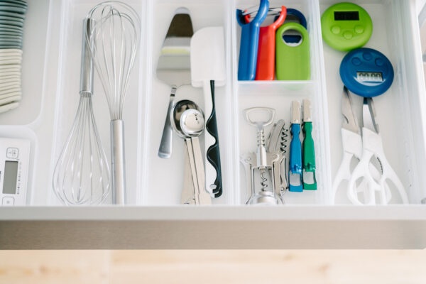 Drawer full of kitchen tools: whisk, spatulas, corkscrew, can opener, bottle openers, scissors, and measuring timers organized in compartments.