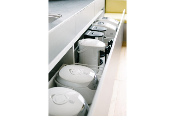 Row of white electric rice cookers stored in a pull-out kitchen drawer.