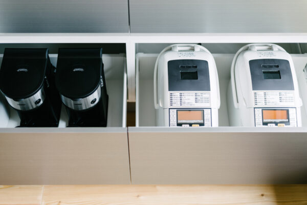 Two black coffee grinders sit in a cabinet beside two white coffee vending machines in a modern kitchen area.