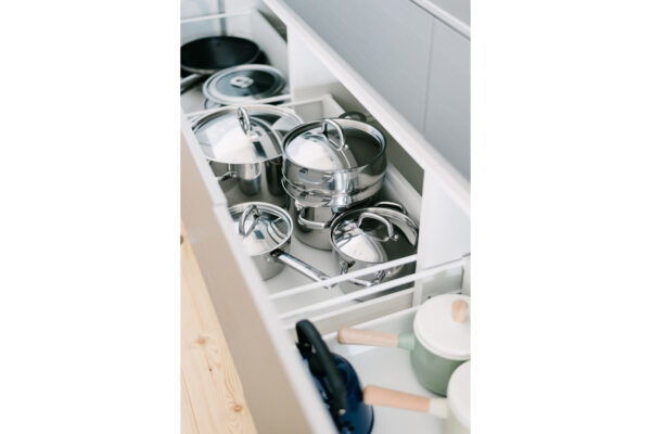Stainless steel pots with lids stored in an open kitchen pull-out drawer inside a modern kitchen cabinet