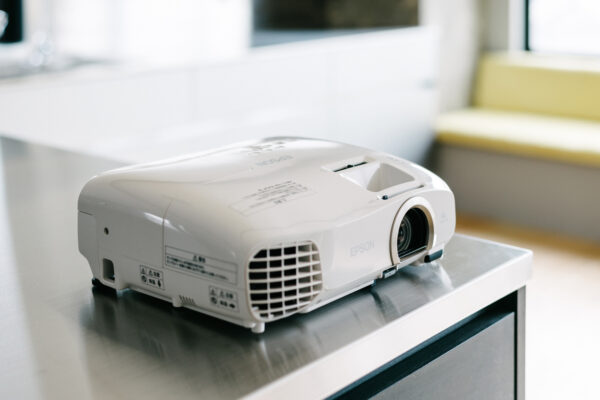 White Epson projector resting on a stainless table in a bright room, ready to project.