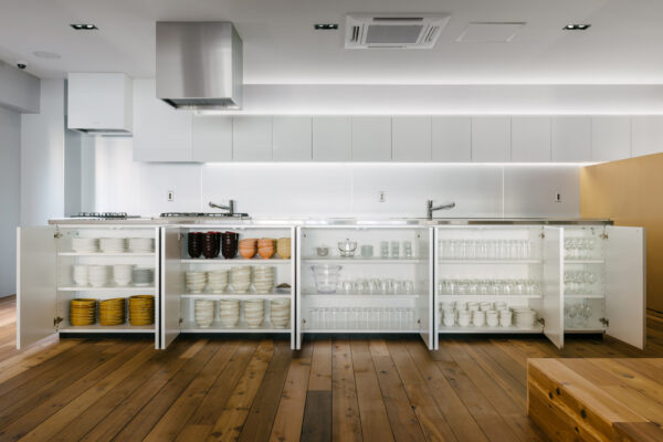 Modern kitchen with open white cabinets displaying bowls, plates, and glassware on a wooden floor.