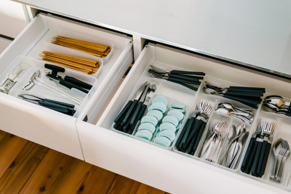 Open kitchen drawer with organized cutlery in separate compartments: forks, knives, spoons, and chopsticks.