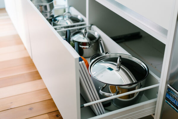 Open kitchen drawer with stainless steel pots, lids, pans, and cutting boards stored inside.