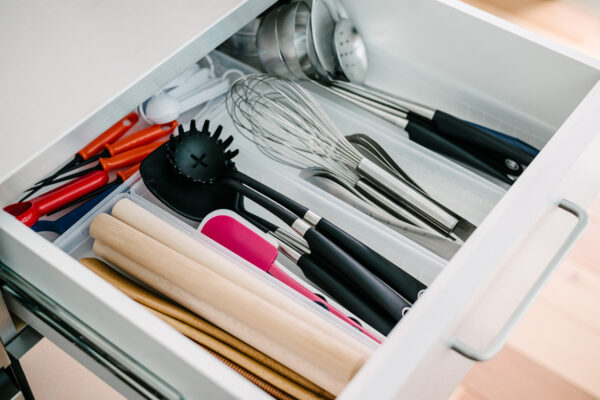Open kitchen drawer containing the cooking utensil set: whisks, spatulas, tongs, ladles, and rolling pins arranged in dividers.