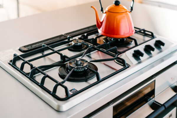 Stainless steel gas stove with an orange kettle on the front burner.