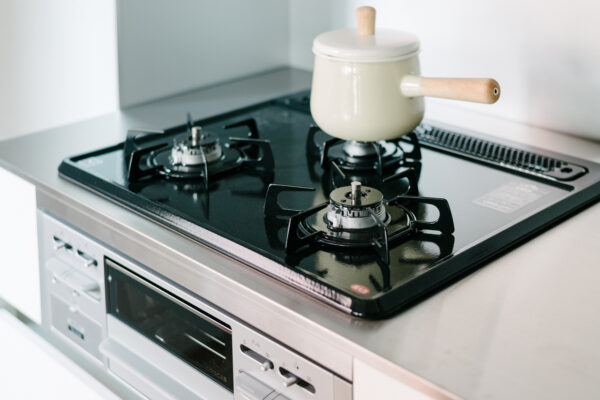 Gas stovetop with three burners on a stainless counter; a beige pot with wooden handles sits on the rear-right burner.