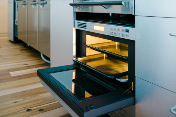 Open stainless steel oven with two racks and warm interior light in a modern kitchen with wooden floor