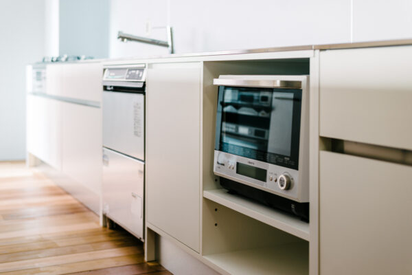 Built-in microwave in a white kitchen cabinet with a dishwasher to the left and hardwood floor visible in the foreground.