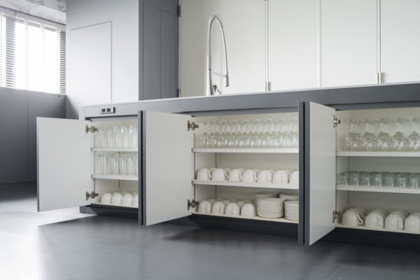 2017_0303_0054 Open kitchen base cabinets reveal glassware, cups, and plates neatly organized on white shelves in a modern kitchen.