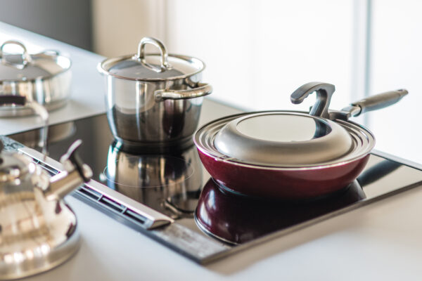 2017_0303_0066 Stainless steel pots with lids sit on a glossy black induction cooktop in a modern kitchen, with a red nonstick pan in the foreground.
