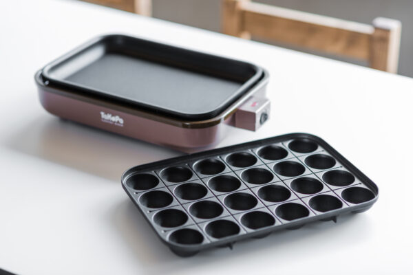 2017_0303_0078 Electric griddle with a rectangular cooking surface and a separate round-well mold tray beside it on a white table.